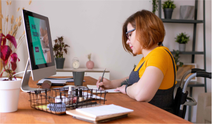 A teacher in a wheelchair sitting at their computer desk, taking notes.
